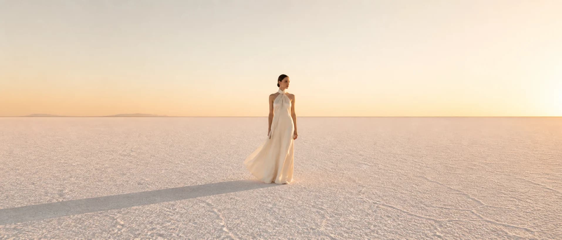 An ultra-wide 21:9 fashion campaign image showing a model on white salt flats with vast negative space.